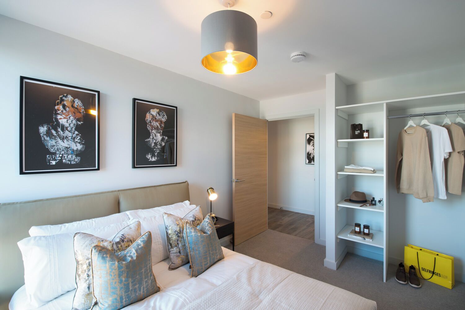 Un dormitorio moderno con una cama, dos obras de arte enmarcadas, un armario y un zapatero colgante.