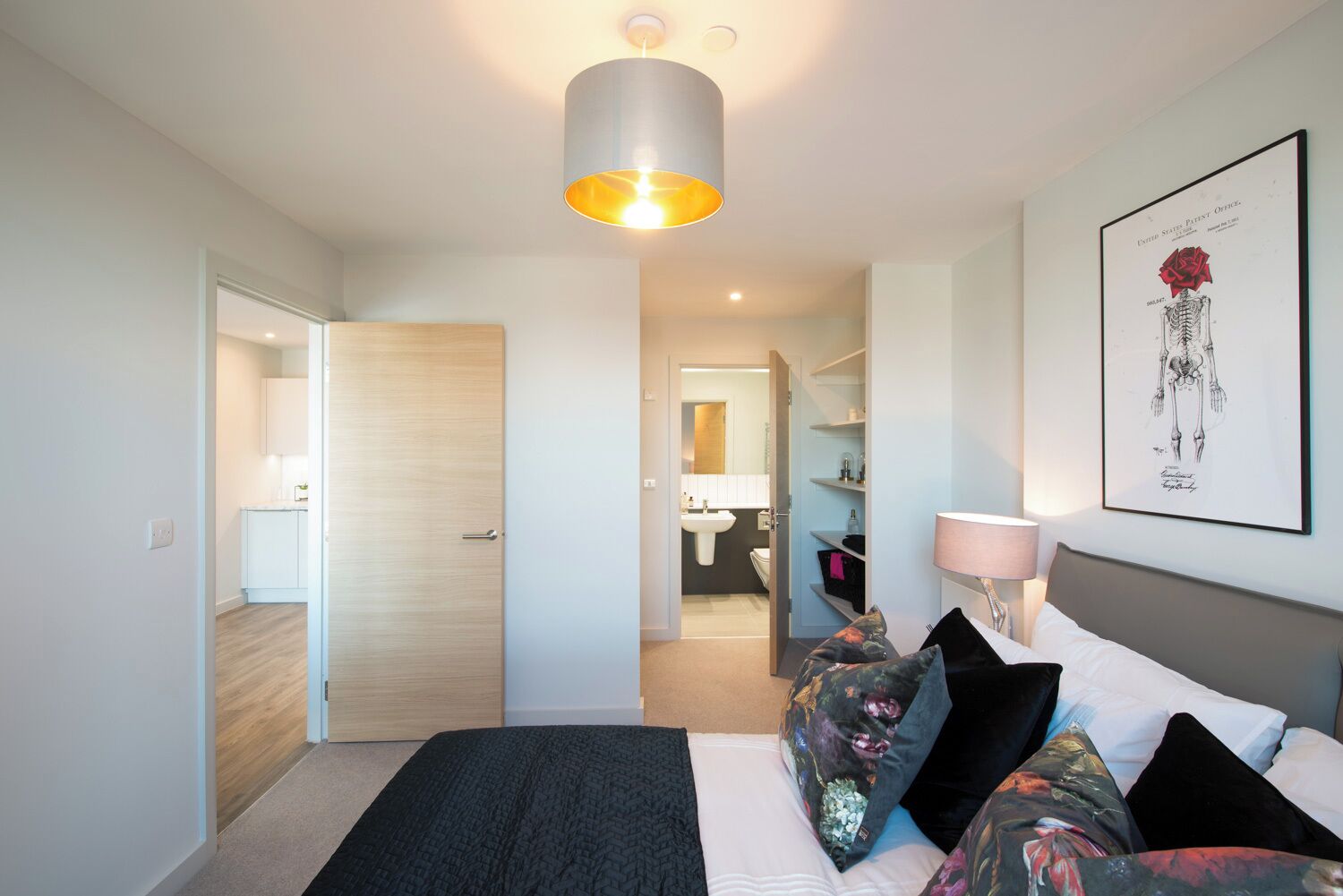 Un dormitorio moderno con cama, lámpara de noche, una obra de arte en la pared y un pasillo que conduce a un baño.
