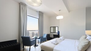 A hotel room with a bed, two chairs, a desk, a mirror, and a view of the city. - Livbnb - 2B in Shams Walk to Beach, w/ Marina View (Dubai)