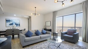 A modern living room with a grey sofa, two armchairs, a glass coffee table, and a dining area with a table and chairs. - Livbnb - 2B in Shams Walk to Beach, w/ Marina View (Dubai)