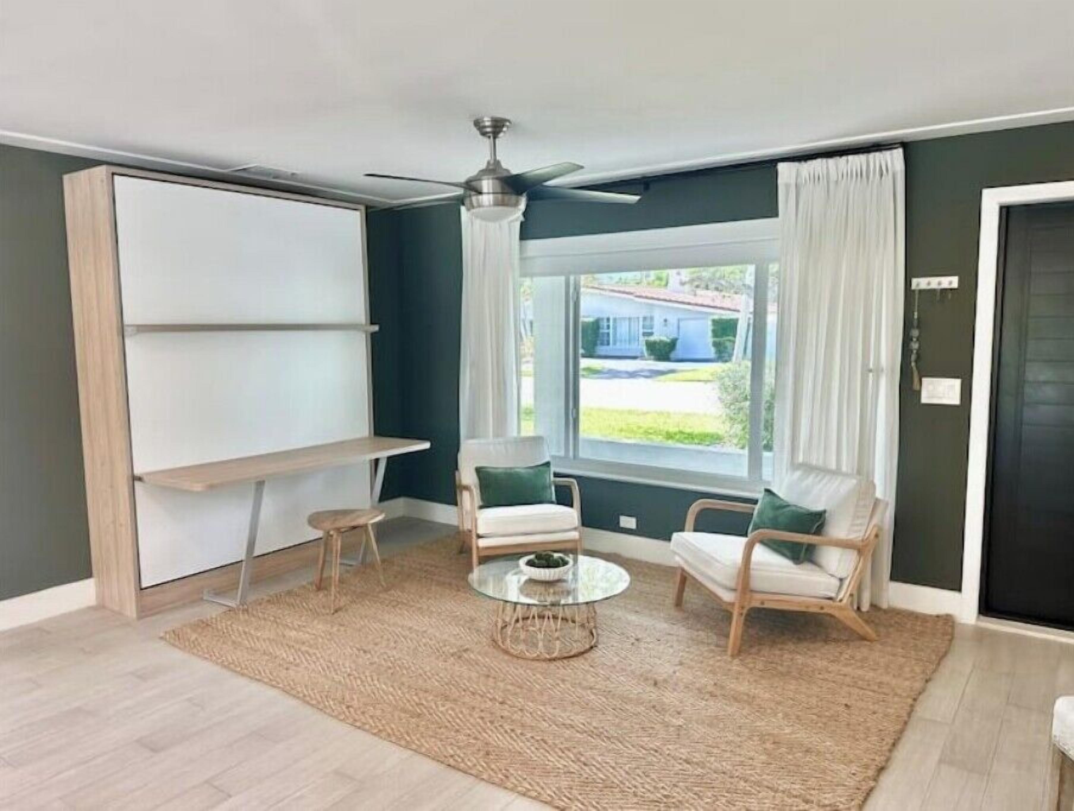 Een moderne woonkamer met een groot raam, een plafondventilator en een ronde salontafel.