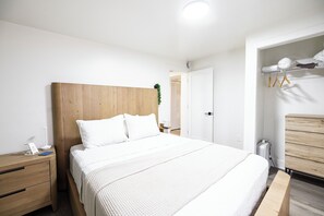 A modern bedroom with a wooden headboard, a neatly made bed, a bedside table with a lamp, and a wooden dresser. - Bridge St Beauty, Brunch & Bars [4 Beds 1 Bath] (Grand Rapids)