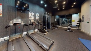 Ein Fitnessstudio mit Laufbändern, Kraftgeräten und einer Spiegelwand.