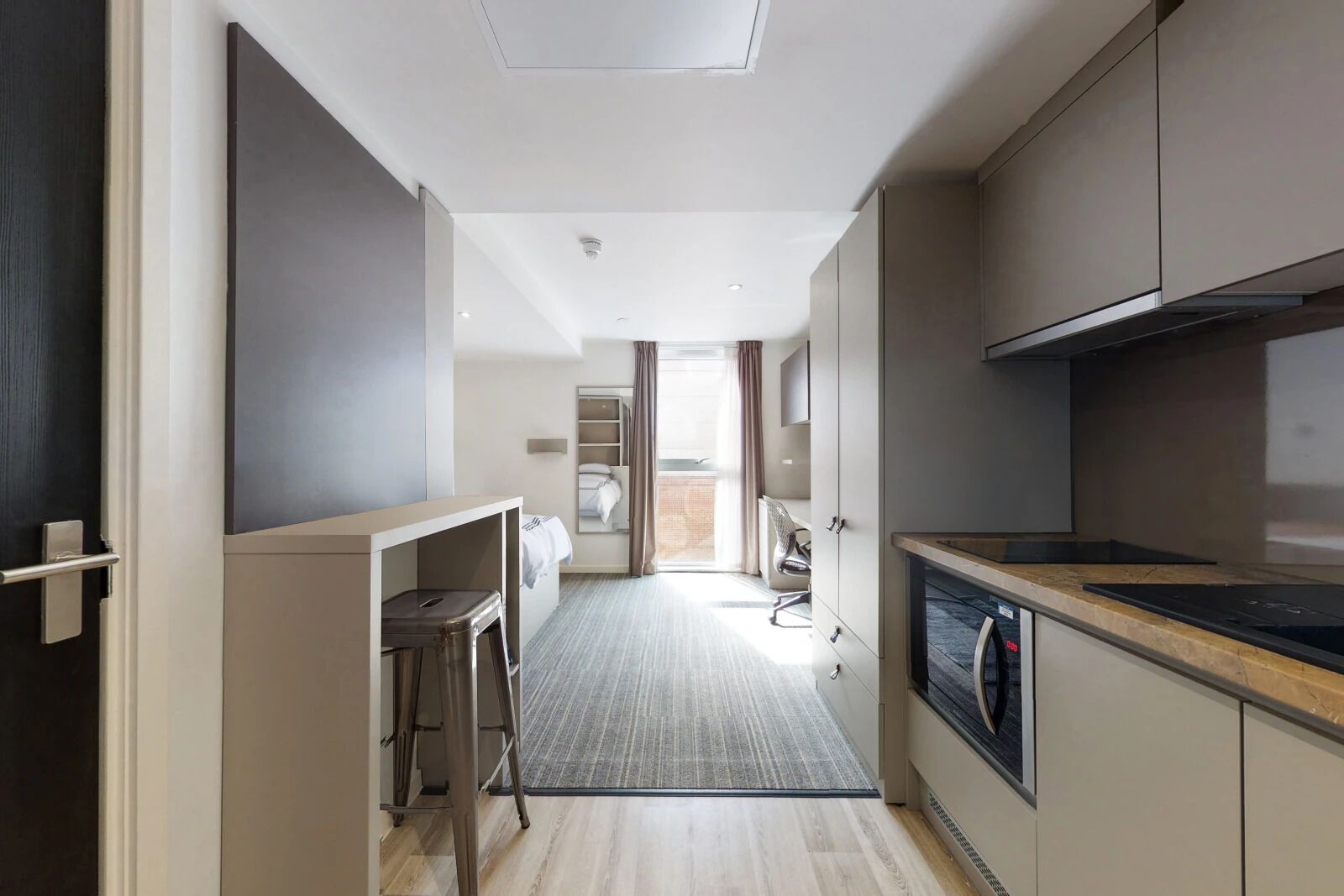 A modern hotel room with a kitchenette, a small seating area, and a view of the outside.