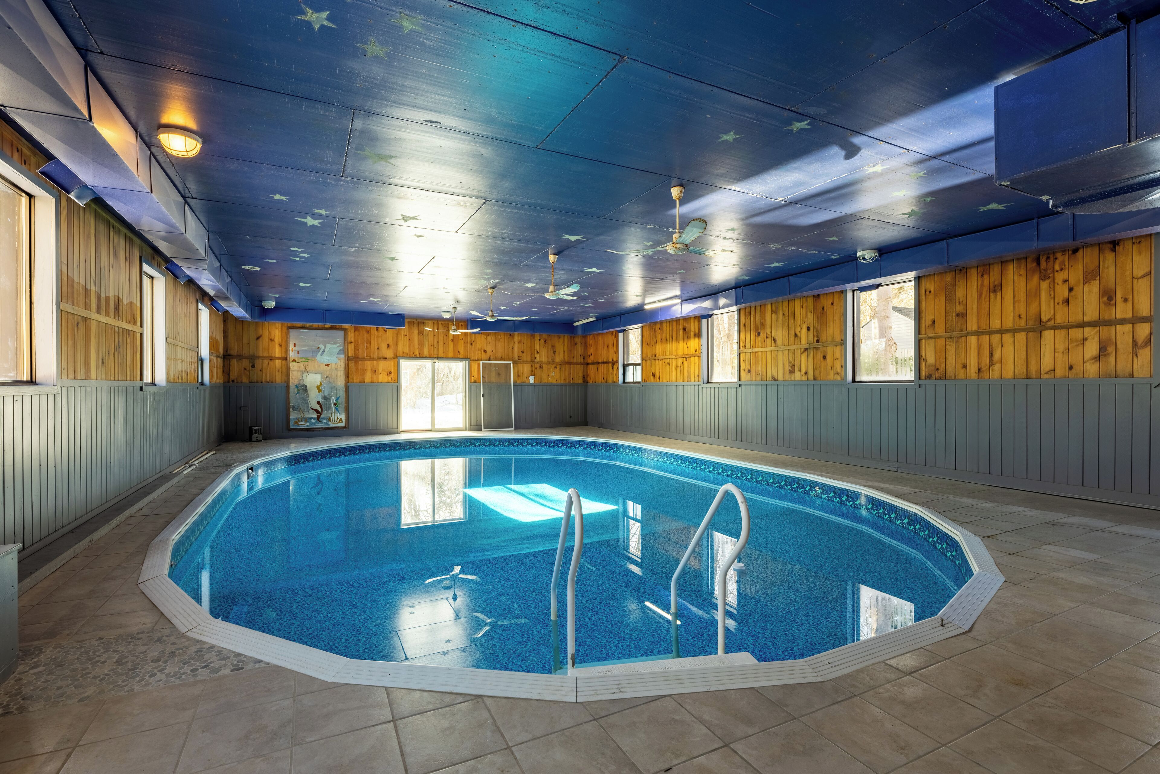 Una piscina interior amb parets de fusta, un terra de rajoles i un sostre pintat amb estrelles.