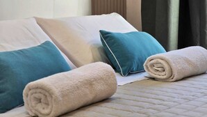 A neatly made bed with pillows and a rolled towel, a bedside table, and a wall-mounted lamp. - O' Vesuvio B&B (Torre del Greco)
