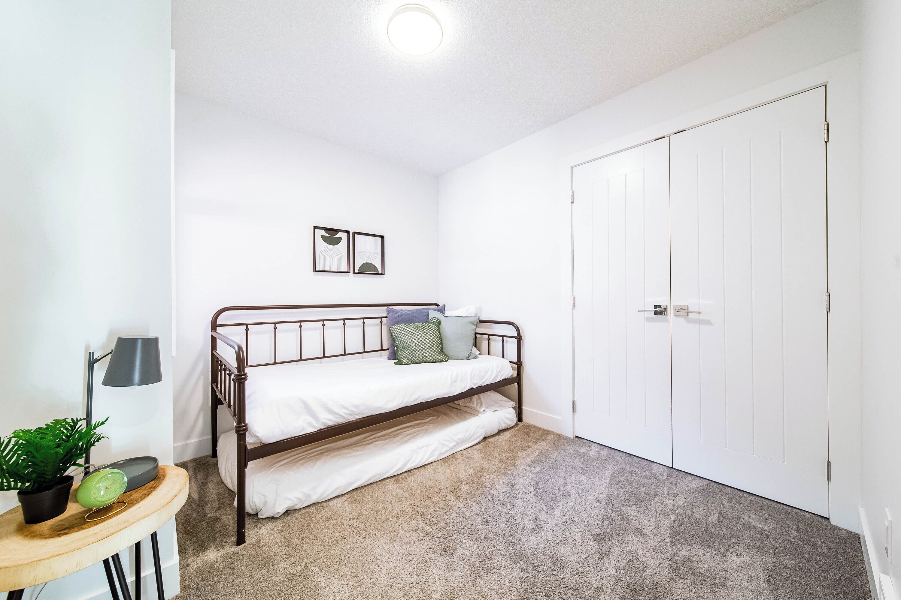 A bedroom with a bunk bed, a bedside table with a lamp, a potted plant, and a door.