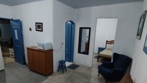 Ein Zimmer mit einer braunen Couch, einem blauen Sessel, einem Holzschrank und einer Mikrowelle.