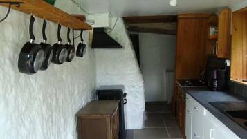 A kitchen with a rustic design, featuring a wooden shelf with hanging pots, a small wooden table, and a black refrigerator.