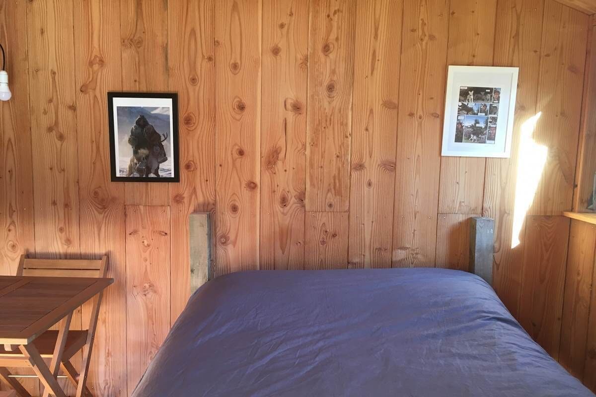 A wooden-paneled room with a bed, a framed photo on the wall, and a small table.