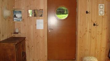 A wooden interior with a round door, a small stool, a shelf with a framed picture, and a wooden cabinet.