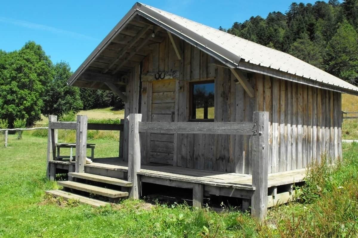 A rustic wooden cabin with a porch and a single window.