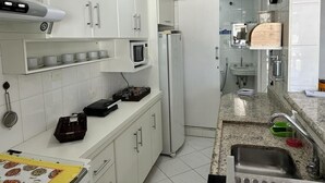 A modern kitchen with white cabinets, a microwave, a refrigerator, and a granite countertop. - Flat Golden Beach (Centro Guarujá)