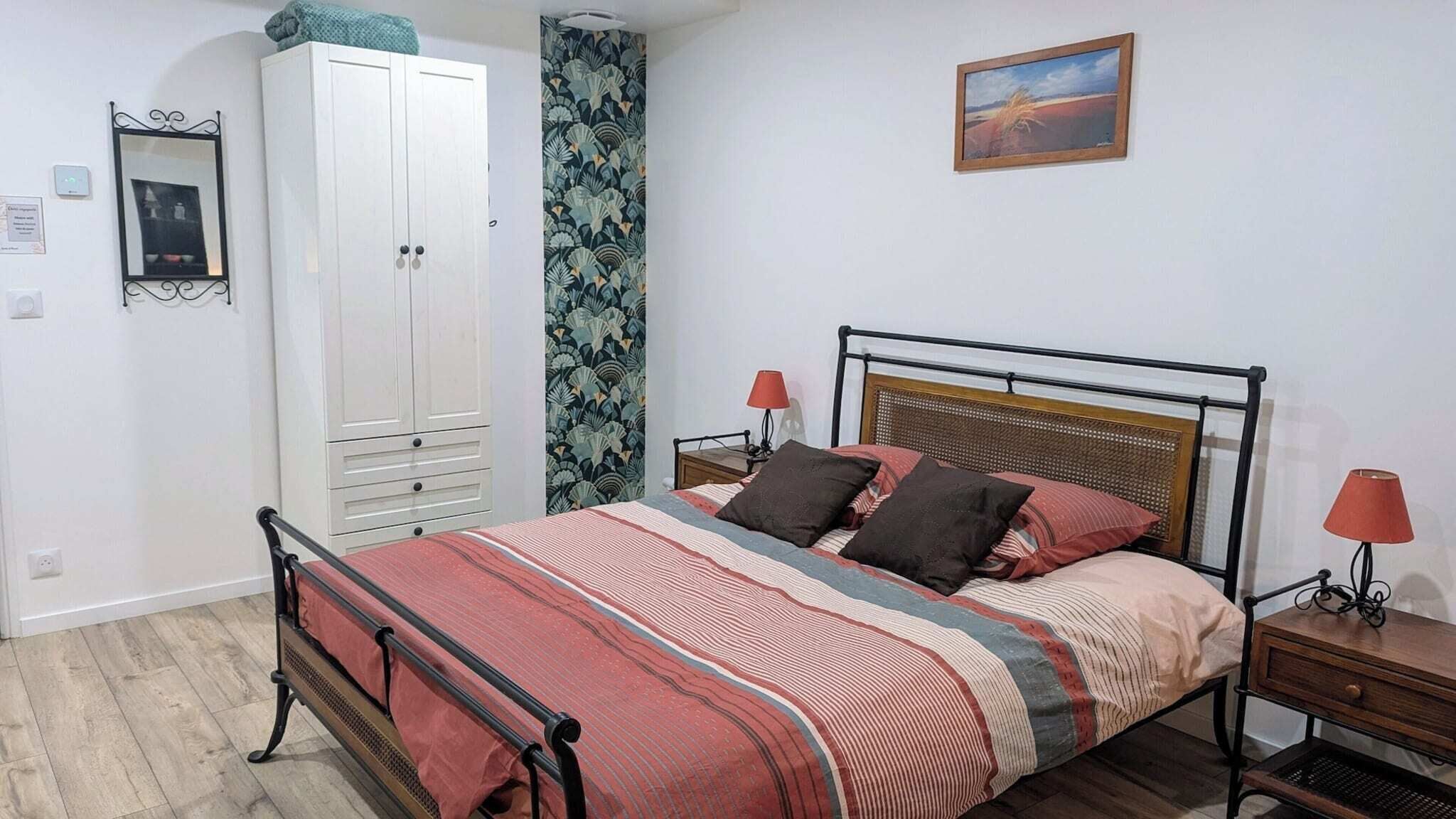 A bedroom with a bed, a wardrobe, a nightstand, a lamp, and a painting on the wall.