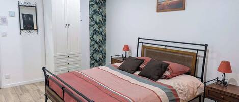 A bedroom with a bed, a wardrobe, a nightstand, a lamp, and a painting on the wall.