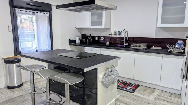 A modern kitchen with a central island, bar stools, a dishwasher, and a coffee machine.