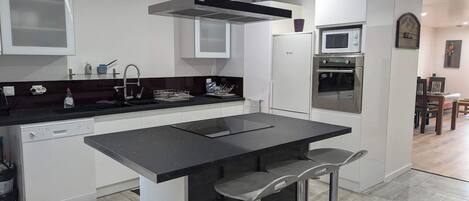 Una cocina moderna con una isla central, electrodomésticos de acero inoxidable y un comedor al fondo.