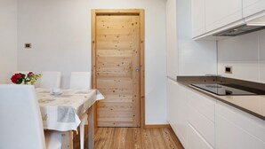 A compact kitchen with white cabinets, a wooden door, and a table with chairs. - Apartment 'Agritur Montibeller Fravort' with Mountain View, Shared Garden and Wi-Fi (Roncegno Terme)