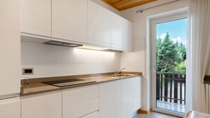 A modern kitchen with white cabinets, a stainless steel countertop, and a window with a view of trees. - Apartment 'Agritur Montibeller Fravort' with Mountain View, Shared Garden and Wi-Fi (Roncegno Terme)