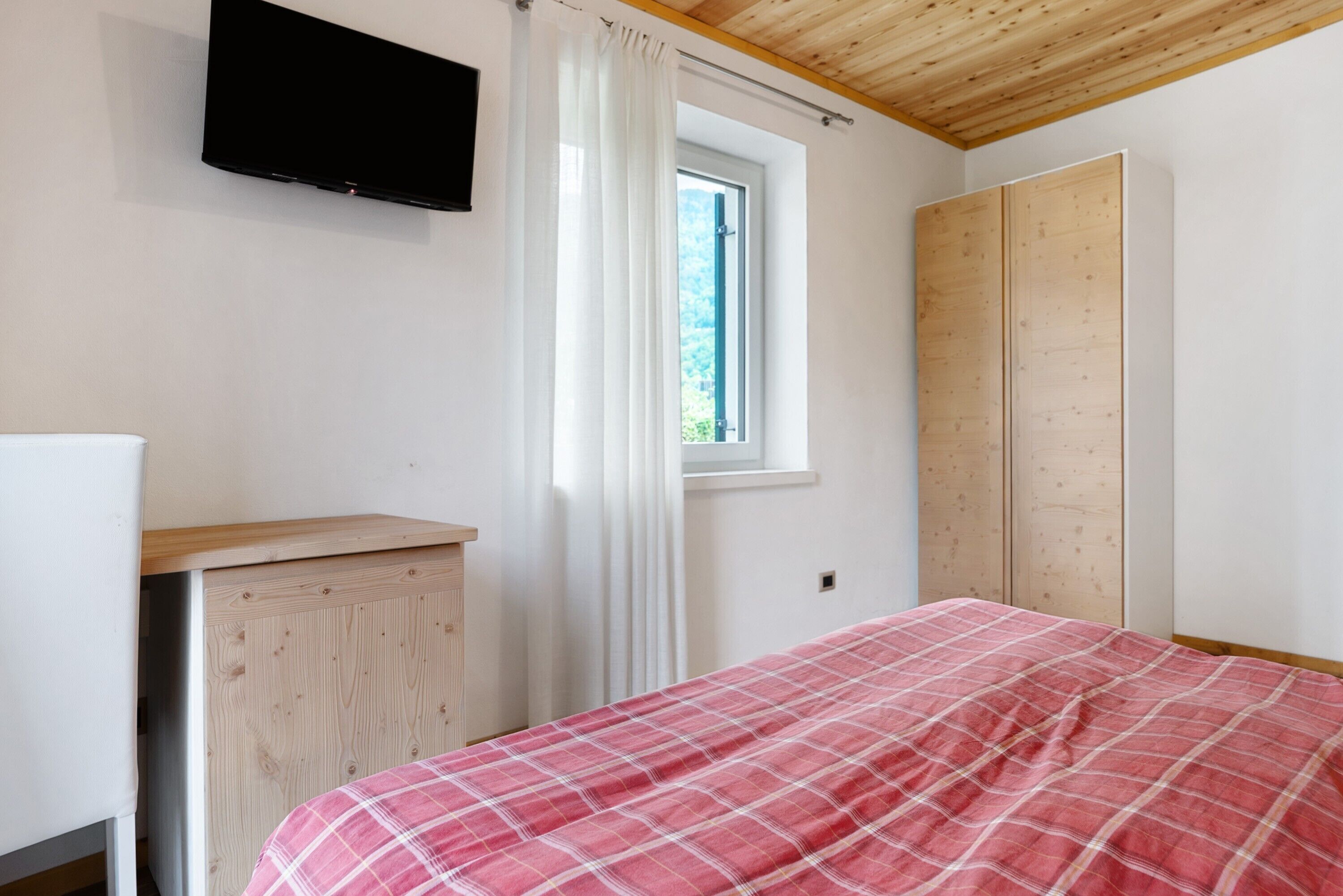 Une chambre à coucher comprenant un lit, une télévision, une fenêtre avec des rideaux et une armoire.