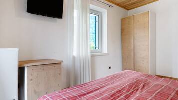 Une chambre à coucher comprenant un lit, une télévision, une fenêtre avec des rideaux et une armoire.