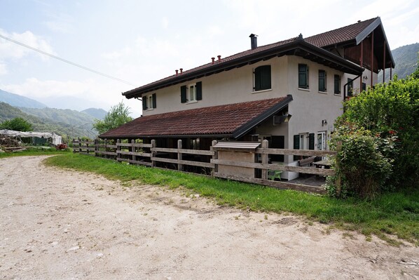 A two-story building with a sloped roof, a wooden fence, and a dirt path leading to it.