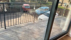 Ein Balkon mit Blick auf eine Wohnstraße, ein rotes Auto und ein blaues Auto, die am Straßenrand geparkt sind.
