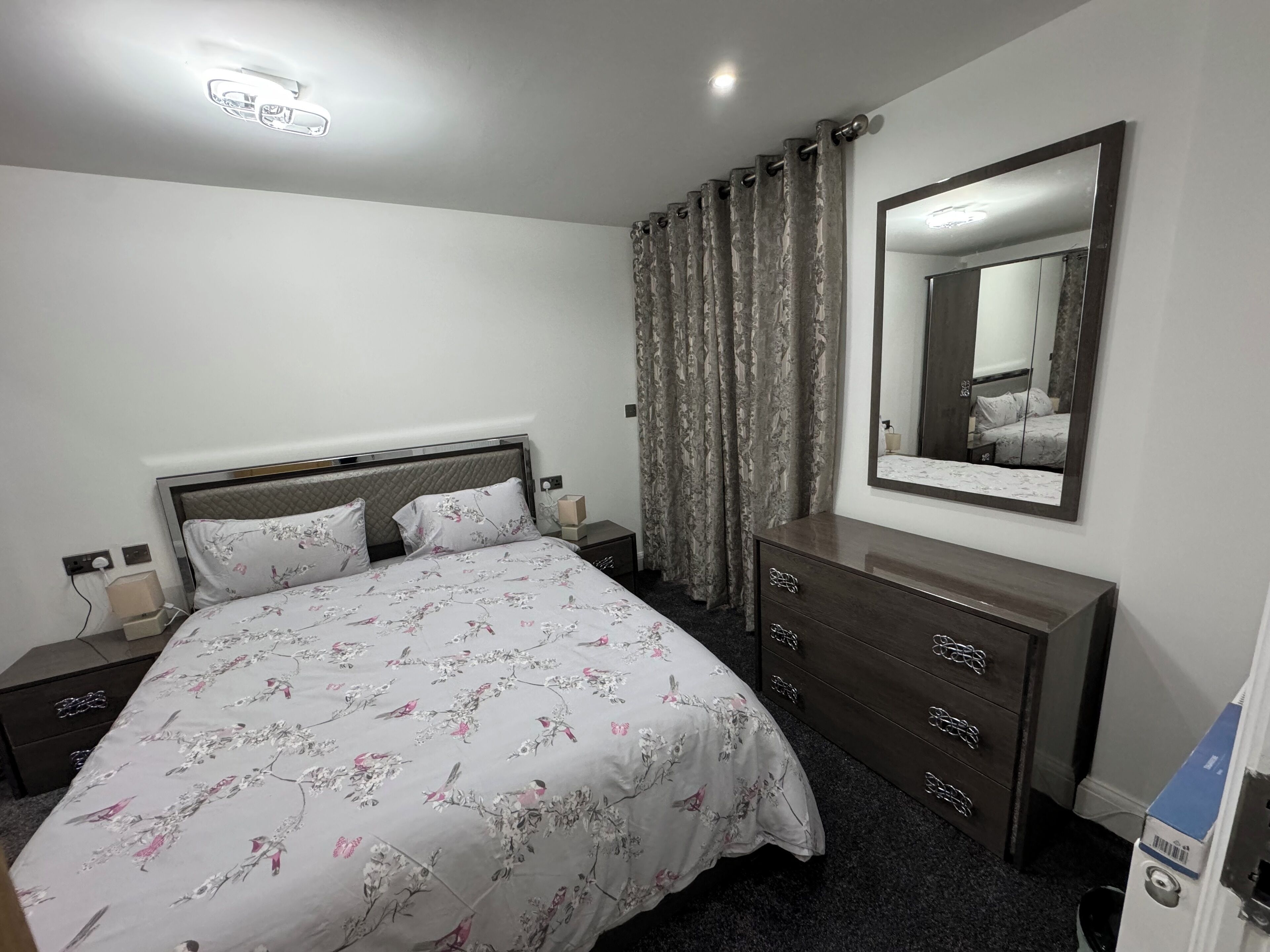 A neatly arranged bedroom with a bed, a dresser, a mirror, and a nightstand.