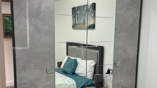 Ein Schlafzimmer mit Bett, Nachttisch und Kleiderschrank mit Spiegel.