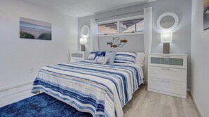 Een slaapkamer met een bed, twee nachtkastjes, een wandspiegel en een schilderij, plus een raam met gordijnen.