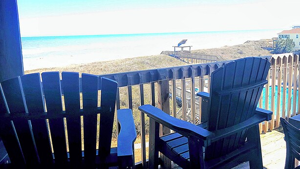 Een balkon met twee Adirondack-stoelen met uitzicht op een strand.