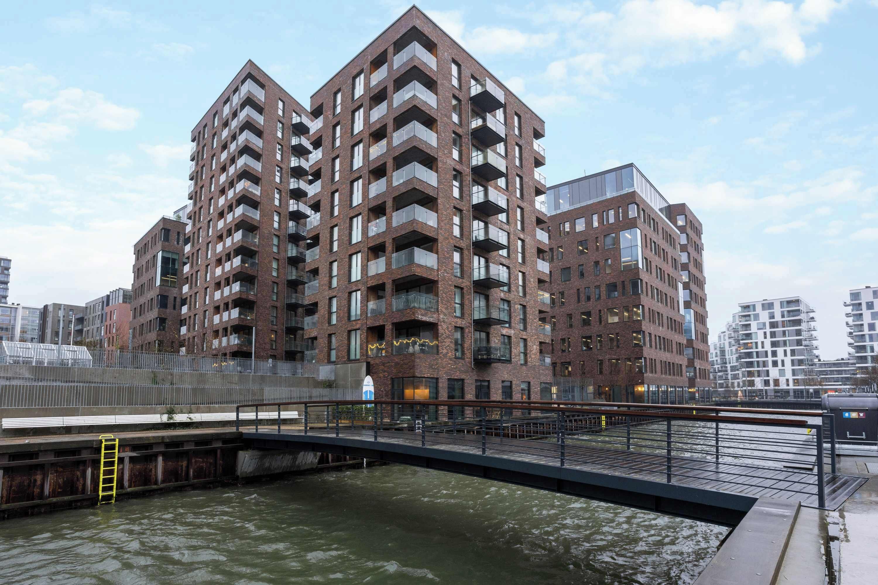 Un edificio residencial alto con múltiples balcones y un puente sobre una masa de agua.
