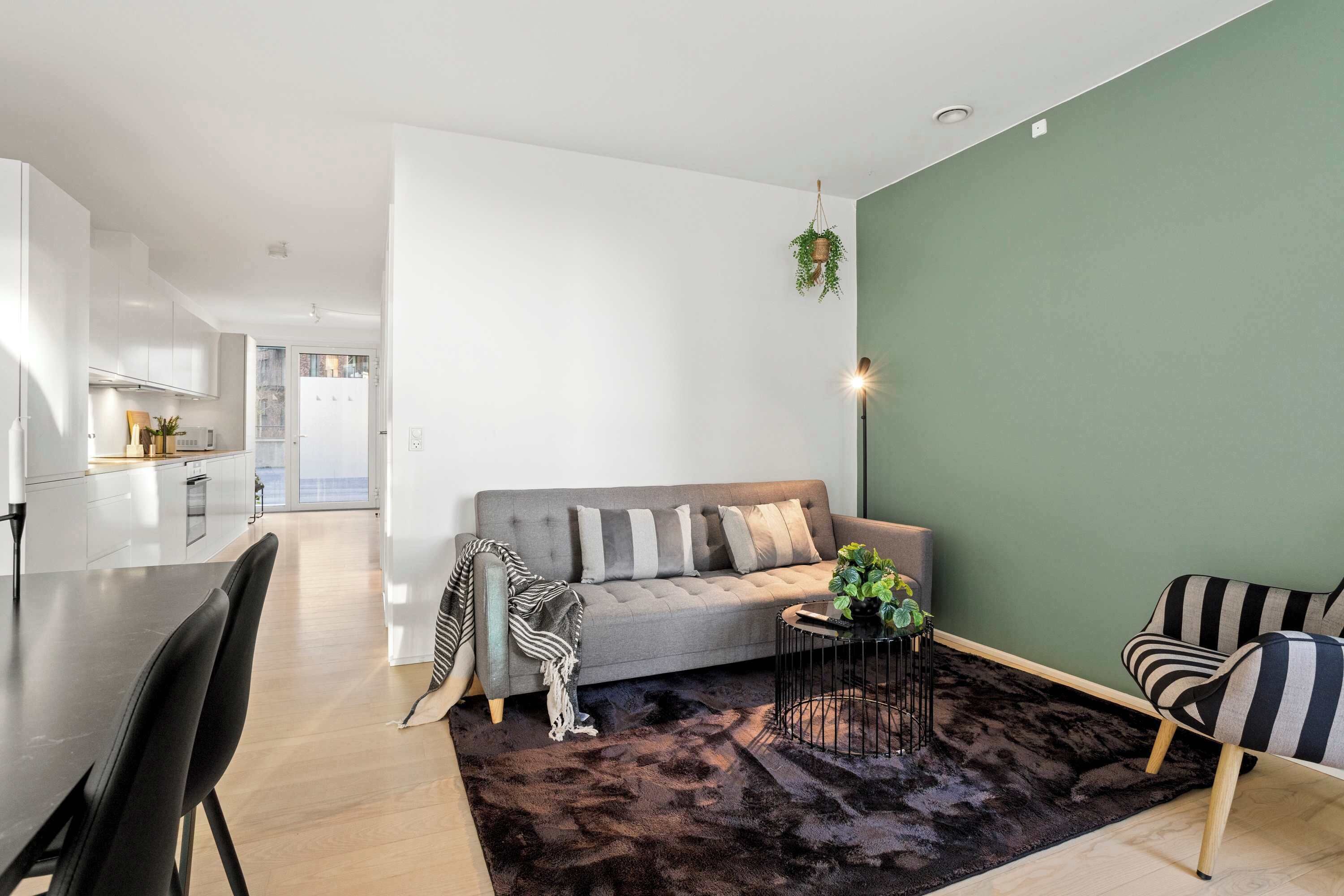 Un salon moderne avec un canapé gris, des fauteuils à rayures, une table basse et un tapis foncé.