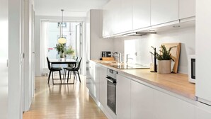 A modern kitchen with white cabinets, a wooden countertop, and a built-in oven. There is a dining area with a table and chairs visible through an open door. - The Iceberg Residence (Aarhus)