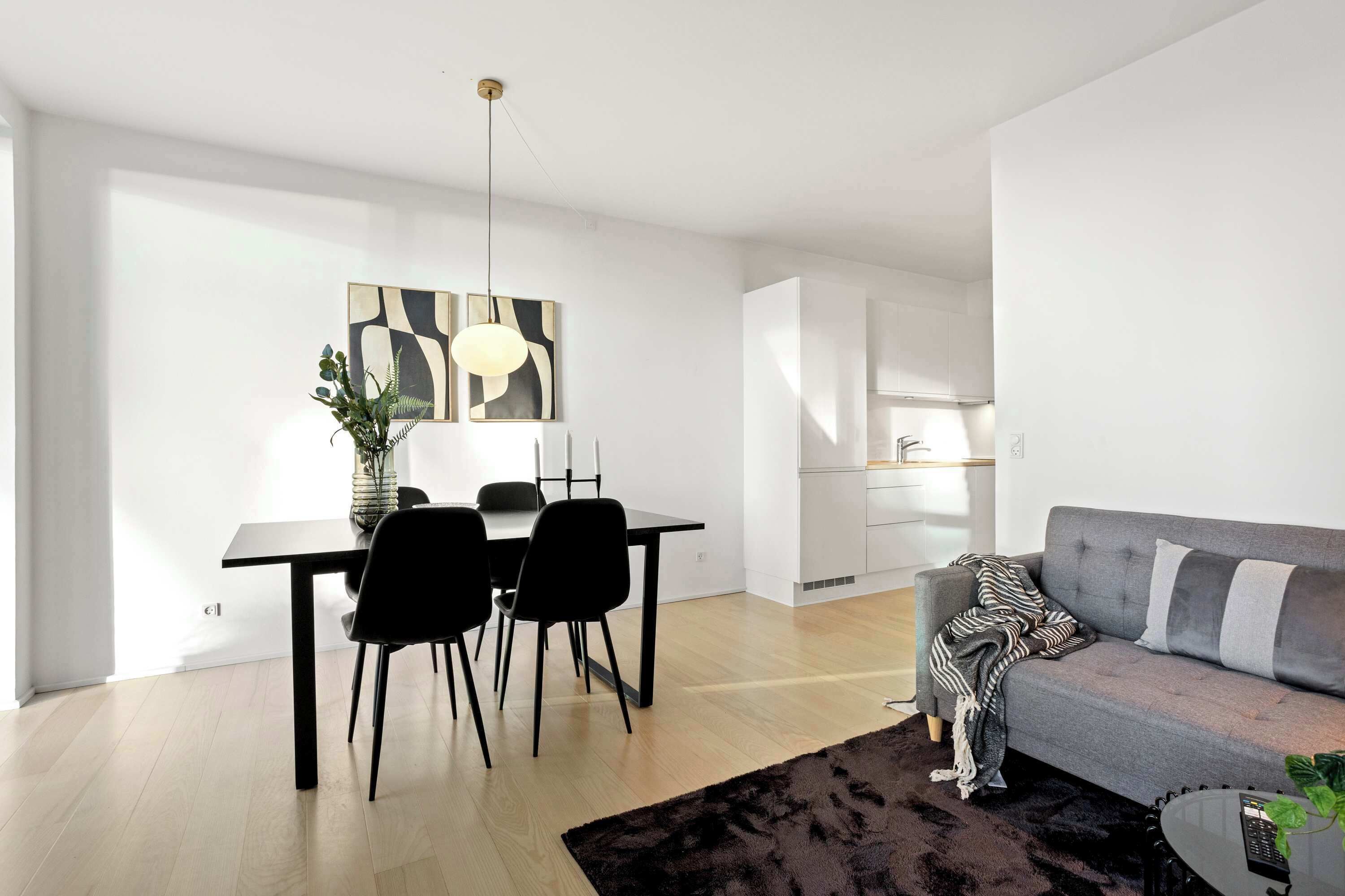 Una sala de estar moderna con un sofá gris, una mesa de comedor con sillas negras y una alfombra negra.