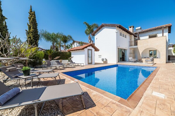 Eine moderne Villa mit Schwimmbad, Außenbereich mit Sitzgelegenheiten und einem gepflegten Garten.