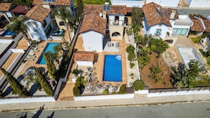 An aerial view of a residential property with two swimming pools, a patio area with lounge chairs, and a small garden. - Kymma River Villa #4 - Charming Ayia Thekla Getaway (Ayia Napa)