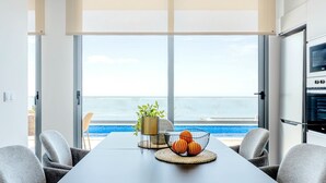 A modern dining area with a view of the ocean, a table with a fruit bowl, and a potted plant. - Villa Serenity - Pool & Sea View (Prazeres)
