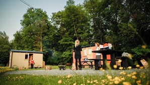 A rustic outdoor setting with a small wooden structure, a wheelbarrow, and a table with items on it. - Cosy en suite shepherd hut on the grounds of Historic building Samlesbury Hall (Samlesbury)