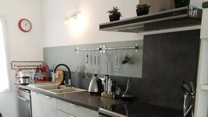 Een moderne keuken met een roestvrijstalen fornuis, een inbouwoven en een zwart aanrecht. Boven de gootsteen hangt een pannendroger en op het aanrecht staat een kleine potplant.
