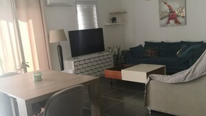 Een moderne woonkamer met een bank, een salontafel, een televisie en een eethoek met stoelen en een tafel.