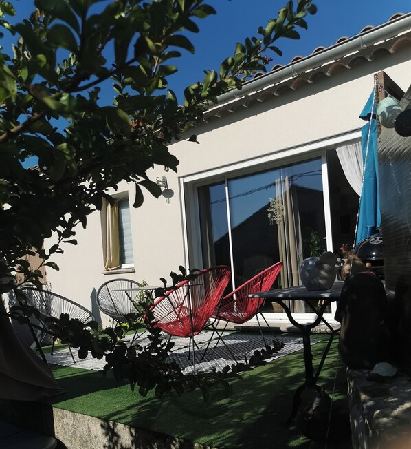 A patio area with a table and two red chairs, a large window, and a blue umbrella. - New single-story house in the village center (Bédoin)