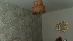Een slaapkamer met een bed, een houten hoofdbord, witte kussens, een nachtkastje, een dressoir, een spiegel en een muur met een bladmotief.