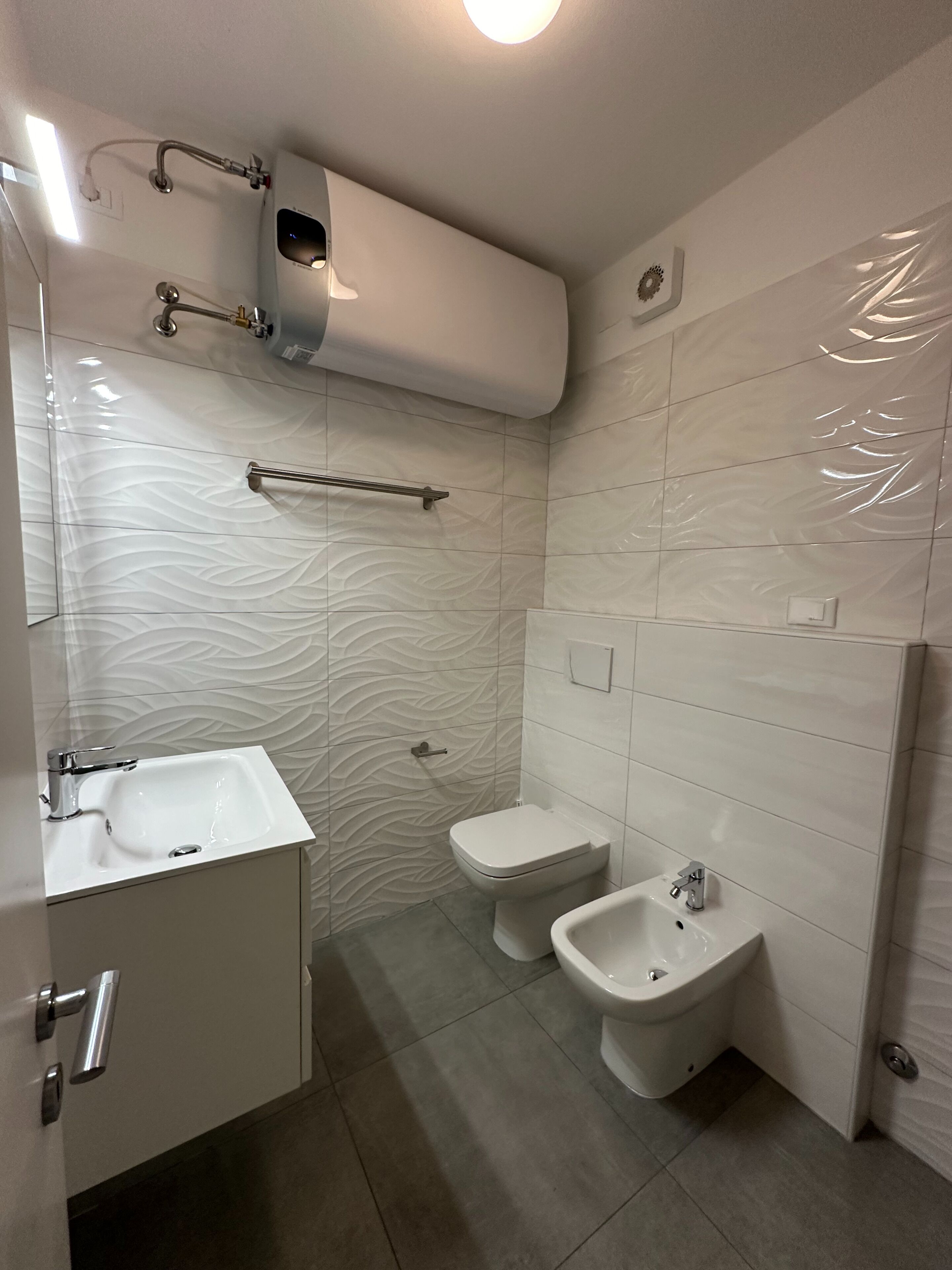 Une salle de bain moderne avec un lavabo blanc, deux bidet, des toilettes et un porte-serviettes.
