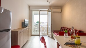 A modern kitchen with a refrigerator, a flat-screen TV, and a dining area with a table, chairs, and a striped sofa. - Bright Flat Near the Beach in Bibione (San Michele al Tagliamento)