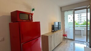 A compact kitchen with a red refrigerator, a microwave, and a wooden cabinet. There is a television on the cabinet, and a sliding glass door leading to an outdoor area. - Bright Flat Near the Beach in Bibione (San Michele al Tagliamento)