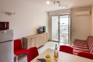 Cozy living space with a kitchenette, flat-screen TV, and dining area, leading to a balcony with outdoor seating.