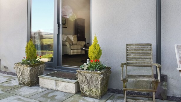 A building entrance with a sliding glass door, two potted plants, and a wooden bench. - The Wolfs Den - UK49083 (Laneshawbridge, near Colne)