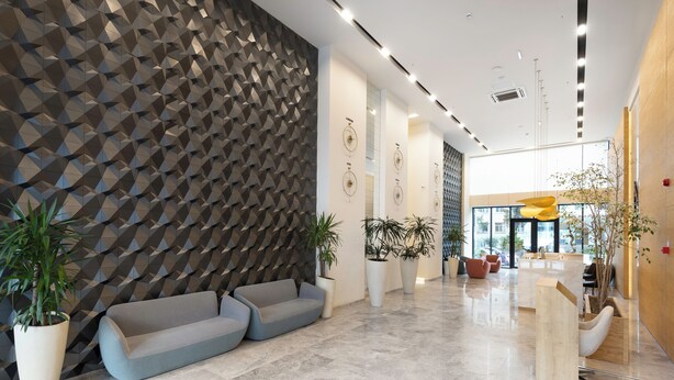 Een moderne lobby met een geometrisch wandontwerp, zithoeken en potplanten.