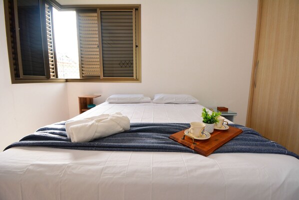 A neatly made bed with white linens, a blue throw blanket, and a tray with a cup and a small plant.